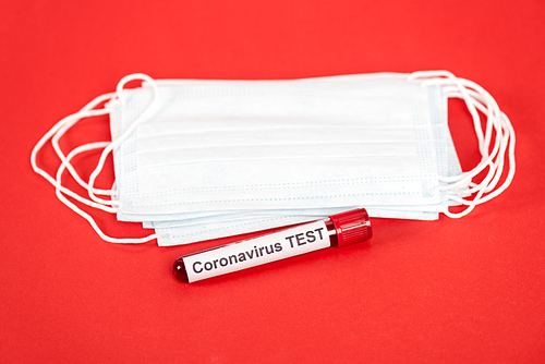 sample with coronavirus test lettering near protective medical masks isolated on red
