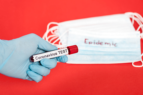 cropped view of scientist holding sample with coronavirus test lettering near medical masks isolated on red