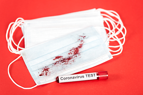 selective focus of sample with coronavirus test lettering near medical masks with blood on red