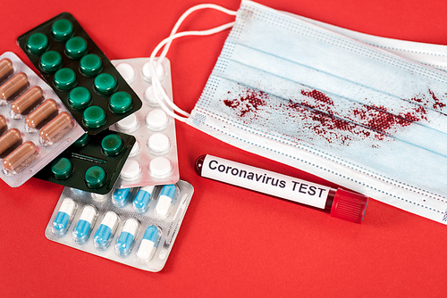 sample with coronavirus test lettering near pills and medical mask with blood on red