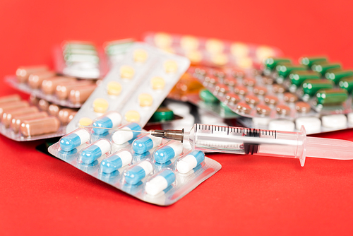 selective focus of syringe near pills in blister packs on red