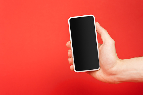 cropped view of man holding smartphone with blank screen isolated on red