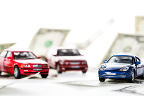 close-up view of small car models and dollar banknotes on white