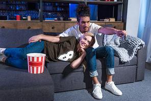 young multiracial couple with popcorn watching film on sofa together at home