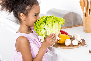 african american child sniffing green lettuce in kitchen