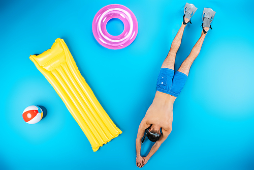 top view of young man diving with flippers and beach items on blue