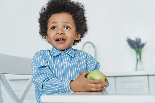 adorable african american boy holding apple at table at home