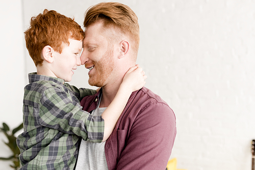 side view of happy red haired father and son hugging at home