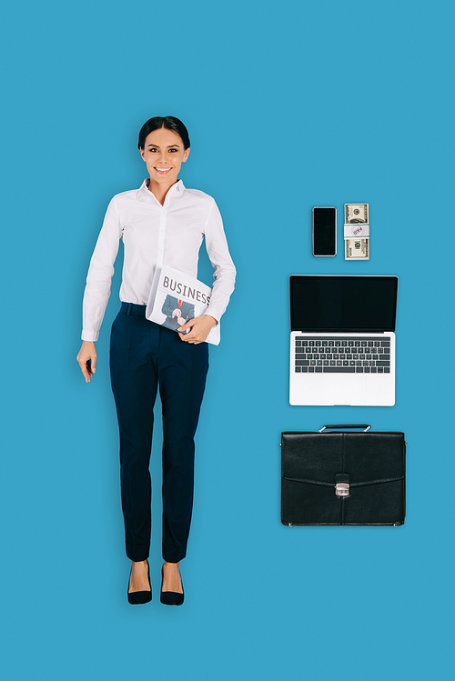 top view of businesswoman with newspaper, briefcase, laptop, smartphone and money isolated on blue background