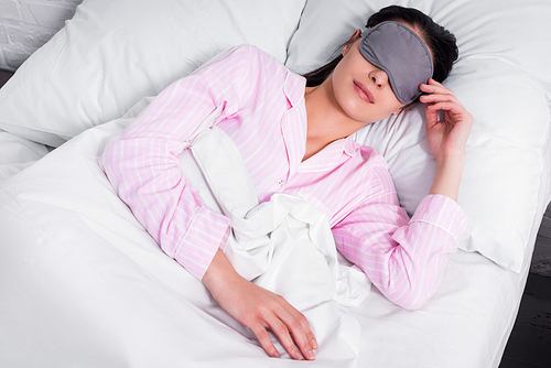 portrait of woman in pink pajamas and sleeping mask sleeping in bed at home