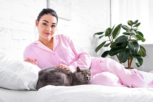 smiling woman with britain shorthair cat lying on bed at home