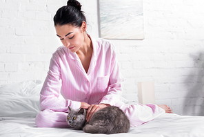 woman in pajamas with britain shorthair cat resting on bed at home