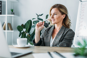attractive businesswoman biting glasses and looking away in office
