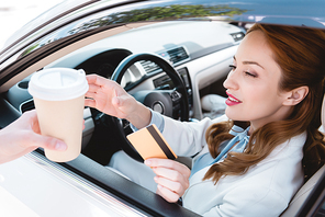 businesswoman with credit card in hand taking coffee to go while sitting in car