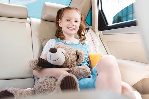 portrait of smiling child with juice and teddy bear in car