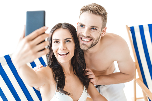 beautiful smiling couple taking selfie with smartphone on beach chairs, isolated on white