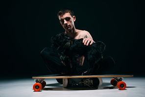 Man with tattoos stroking black dog on longboard on dark background