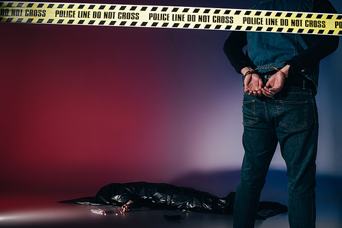 Rear view of murderer in cuffs behind police line on dark background