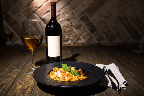 close up view of fettuccine pasta, wine and cutlery on napkin on wooden tabletop