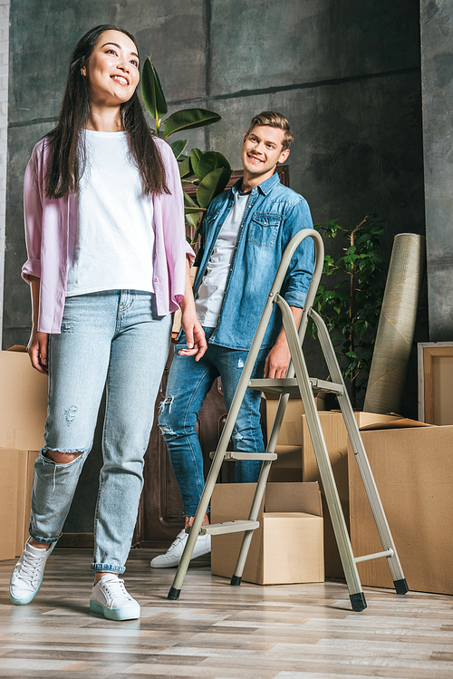 beautiful young couple with boxes and ladder moving into new home