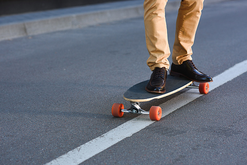 cropped shot of young man standing on skateboard on street