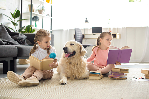 little sisters reading books with golden retriever dog near by at home