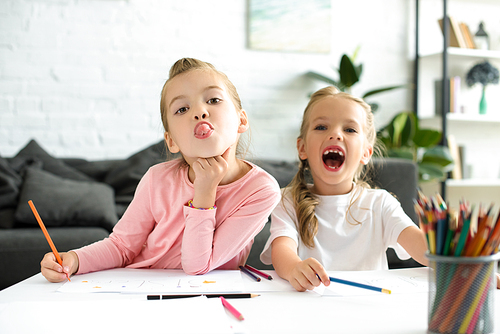portrait of adorable sisters grimacing while drawing pictures at home