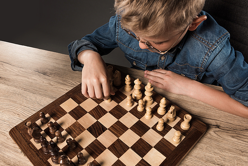 elevated view of little boy in eyeglasses playing chess at table