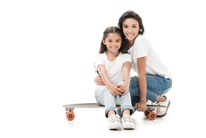 mother sitting near smiling daughter on skateboard isolated on white