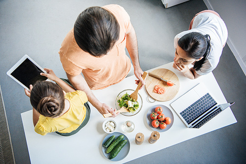 high angle view of young family with gadgets cooking together at kitchen