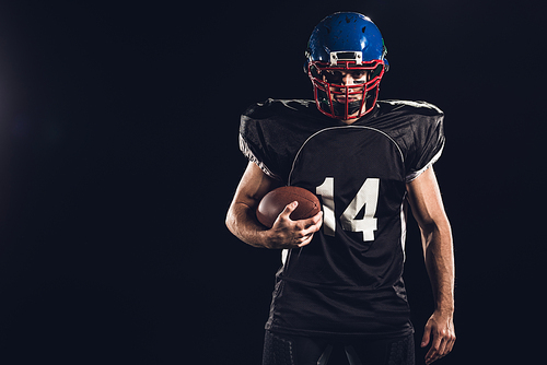 confident american football player holding ball in hand and  on black