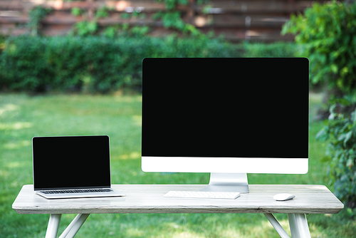 selective focus of laptop and computer with blank screens at table outdoors