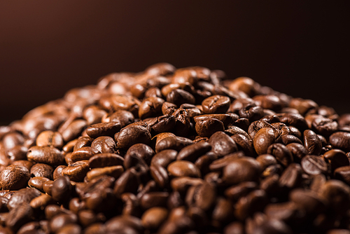 close-up shot of heap of roasted coffee beans on dark brown background