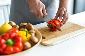 cropped shot of man cutting bell pepper on wooden cutting board
