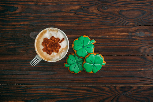top view of cappuccino and cookies in shape of shamrocks on wooden table