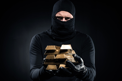 Man in balaclava holding gold bullions in his hands