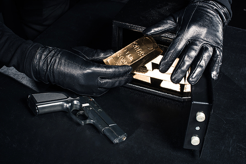 Close-up view of robber with gun taking gold bars from safe