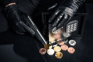 Close-up view of robber with gun stealing bitcoin from safe