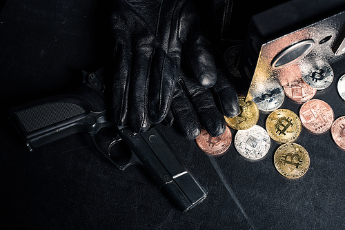 Black gloves and gun by open safe with bitcoin