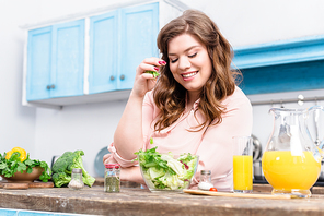 overweight smiling woman at table with fresh salad in kitchen at home