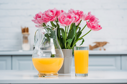 Front view of orange juice and vase with pink tulips on table in modern kitchen