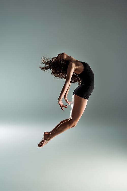 side view of dancer in black bodysuit dancing contemporary on grey background