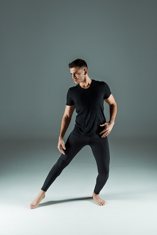 handsome dancer in black leggings and t-shirt dancing contemporary on dark background