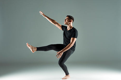 handsome dancer in black leggings and t-shirt dancing contemporary on dark background