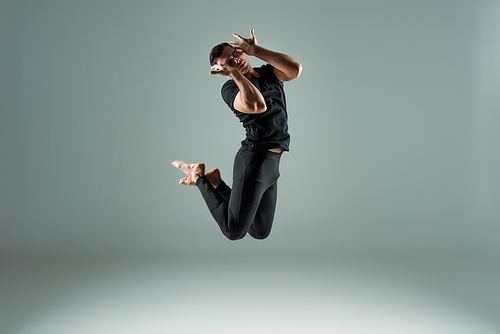 handsome dancer with closed eyes in black leggings and t-shirt dancing contemporary on dark background