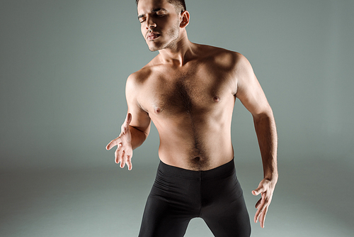 handsome dancer with closed eyes in black leggings dancing contemporary on grey background