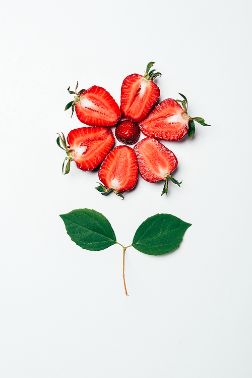 top view of flower made of sliced strawberries and green leaves on white