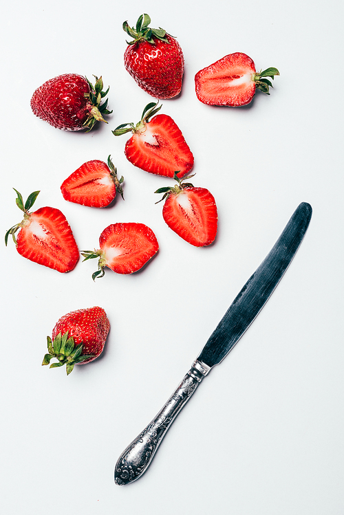 top view of fresh ripe sliced strawberries and knife on white