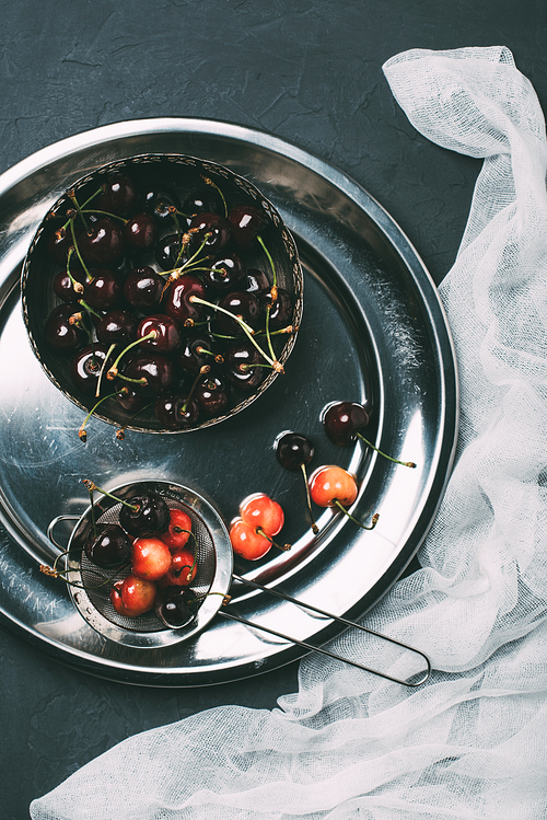 top view of fresh sweet cherries in shiny metal plate on black