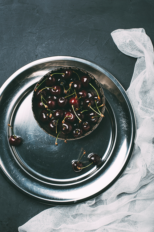 top view of ripe sweet cherries in bowl in shiny metal plate